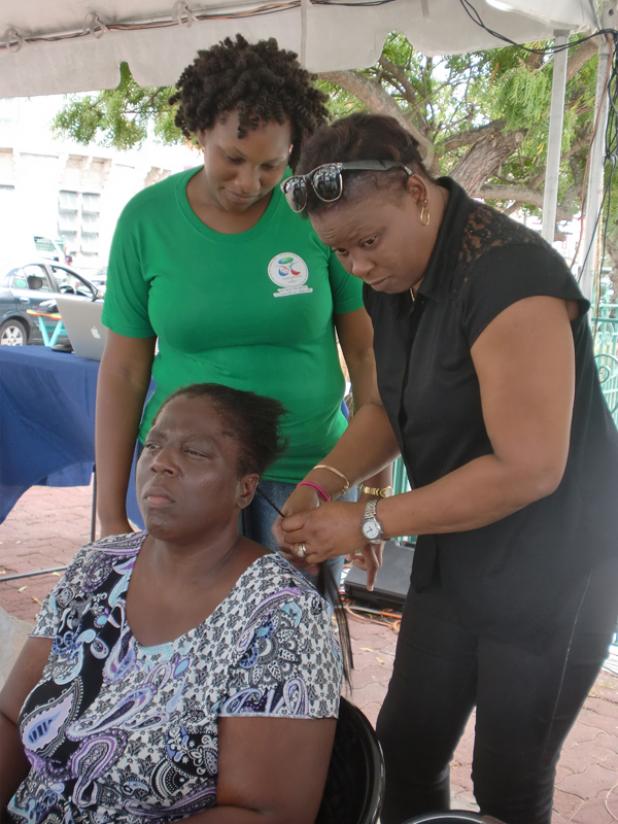 Annmarie Goddard who is visually impaired braiding a client’s hair as Zoe Belgrave, a UWI Social Work student looks on. 