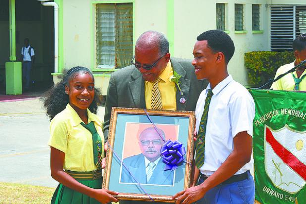 Jeffrey Broomes, outgoing Principal at Parkinson Memorial School, presenting the school with a portrait of himself to be placed in the hall. Receiving it is Headgirl, Tanneil Burnett, and Headboy, Neantro Spencer. 