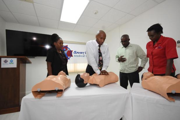 Managing Director of Sandy Crest Medical Centre, Dr. Brian Charles (second from left), gives the CPR training mannequin a few chest compressions, as (extreme left) Head of the Accident & Emergency Department of the Queen Elizabeth Hospital, Dr. Cheynie Williams, Commander David Dowridge of the St. John Ambulance Brigade and CEO of the Heart & Stroke Foundation of Barbados, Gina Pitts, look on.  
