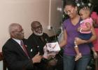 Christine Smith holds her young daughter, Zahra Smith, in her arms, as she collects a Christmas gift on behalf of her daughter from the Governor General of Barbados, His Excellency Sir Elliott Belgrave, on his annual visit to the Queen Elizabeth Hospital (QEH). Looking on is the Chairman of the QEH Board of Management, Joseph King.